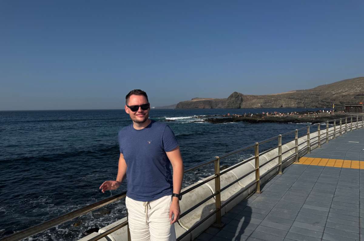 a photo of a tourist smiling on the Agaete seafront promenade with a rugged headland behind, Canary Islands, photo by Next Level of Travel
