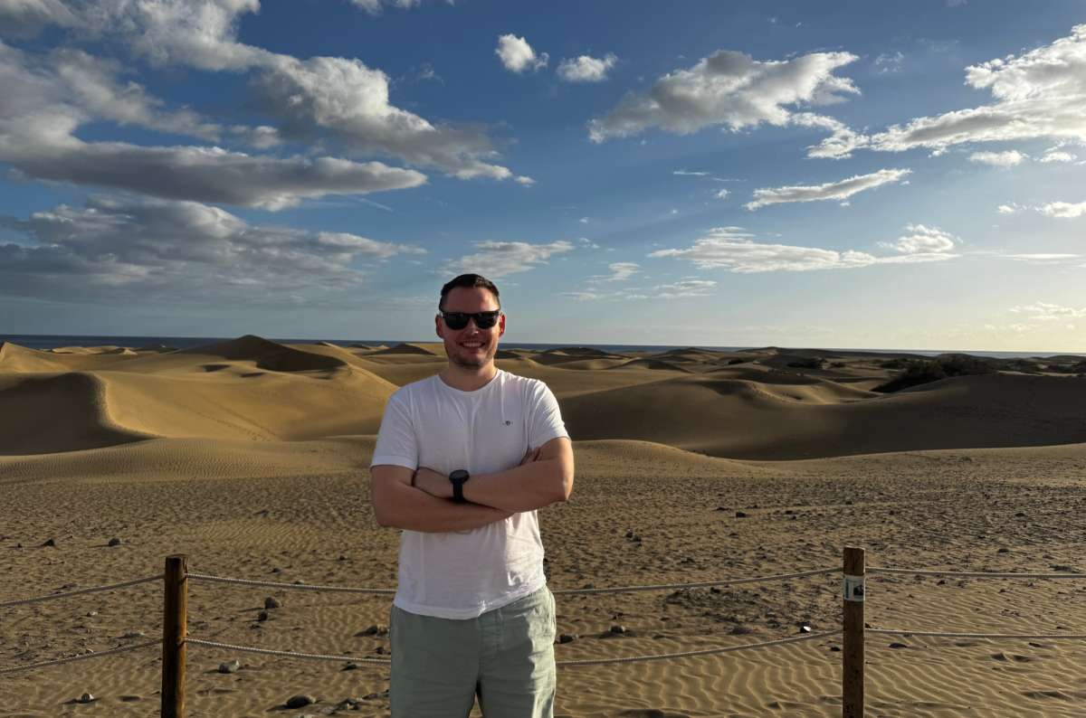 a photo of a tourist standing with arms crossed in front of the golden Maspalomas dunes at sunset, Canary Islands, photo by Next Level of Trave