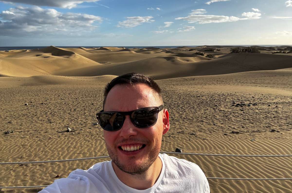 a photo of a tourist taking a selfie in front of the rolling Maspalomas dunes in late afternoon light, Canary Islands, photo by Next Level of Travel