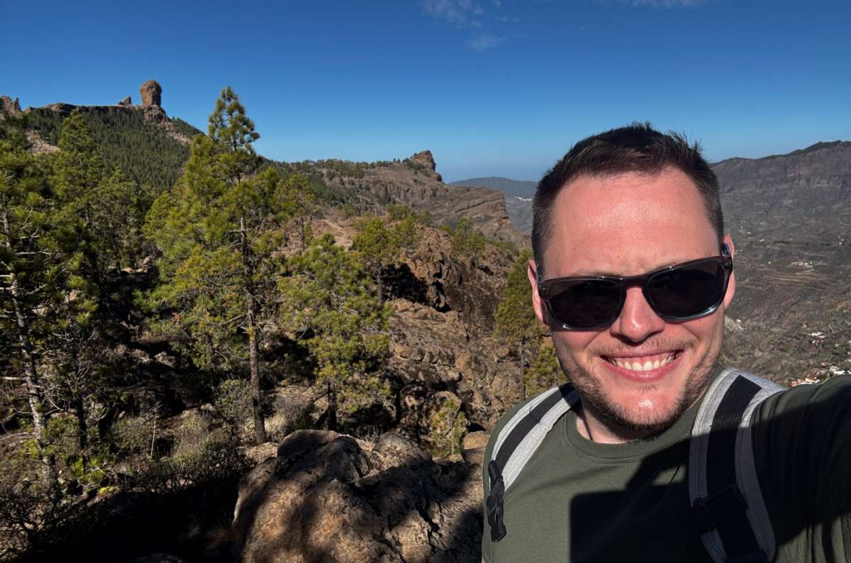 a photo of a tourist taking a selfie on a hiking trail with the Roque Nublo rock formation rising behind, Canary Islands, photo by Next Level of Travel