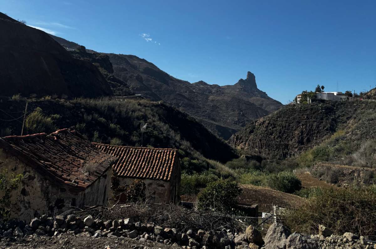 a photo of an old red-tiled stone farmhouse in a valley below the pointed peak of Roque Bentayga, Canary Islands, photo by Next Level of Travel