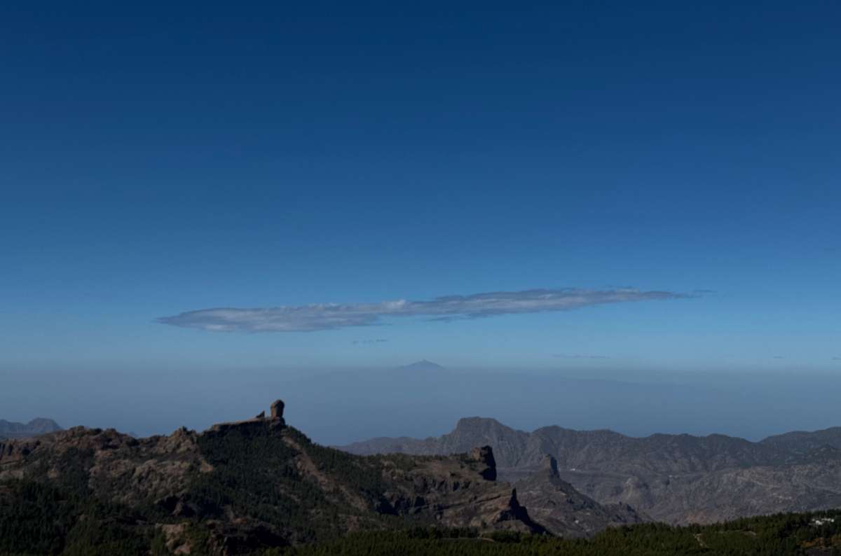 a photo of Roque Nublo on a ridge with Tenerife's Teide rising above the sea haze in the distance, Canary Islands, photo by Next Level of Travel