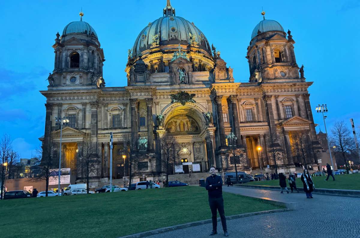 A photo showing a tourist posing in front of the illuminated Berlin Cathedral on Museum Island, Germany, a photo by Next Level of Travel