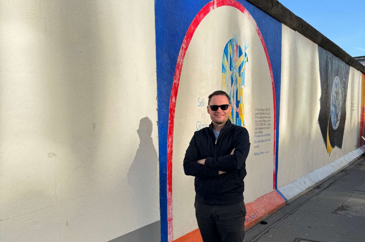 A photo showing a tourist posing in front of the paintings along the East Side Gallery in Berlin, Germany, a photo by Next Level of Travel