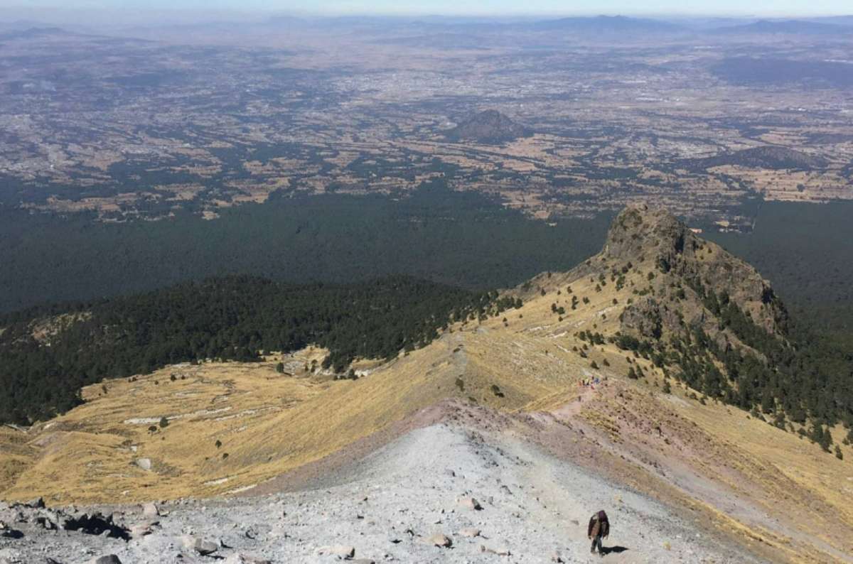 a photo of a hiker on the rocky ridge below La Malinche summit with the plains below, Tlaxcala, Mexico