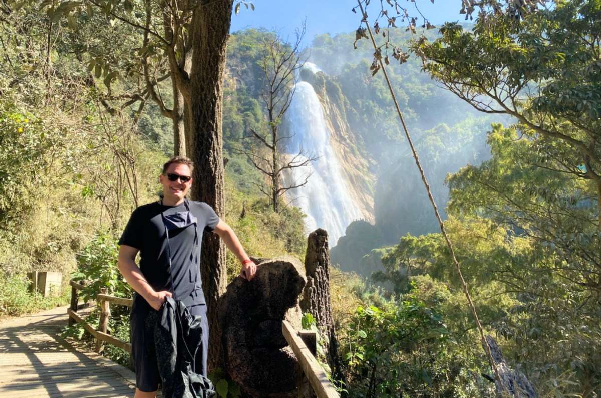 a photo of a tourist leaning on a wooden railing in front of the Velo de Novia waterfall, El Chiflón, Chiapas, Mexico, photo by Next Level of Travel