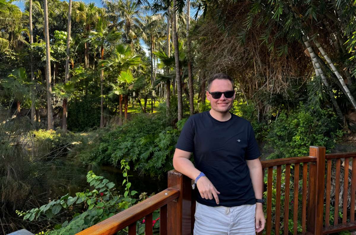 a photo of a tourist posing in front of a railing with green trees visible in the background of the park, Loro Parque, Canary Islands, photo by Next Level of Travel