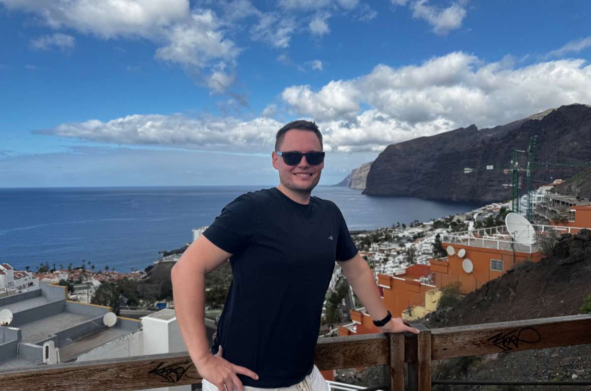 a photo of a tourist posing in front of the view of Los Gigantes, with the city and the sea visible in the background, Canary Islands, photo by Next Level of Travel