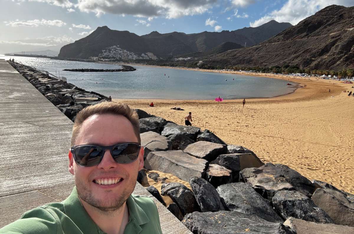 a photo of a tourist taking a selfie at Playa de las Teresitas, with the sandy beach, cliffs and sea visible in the background, Canary Islands, photo by Next Level of Travel