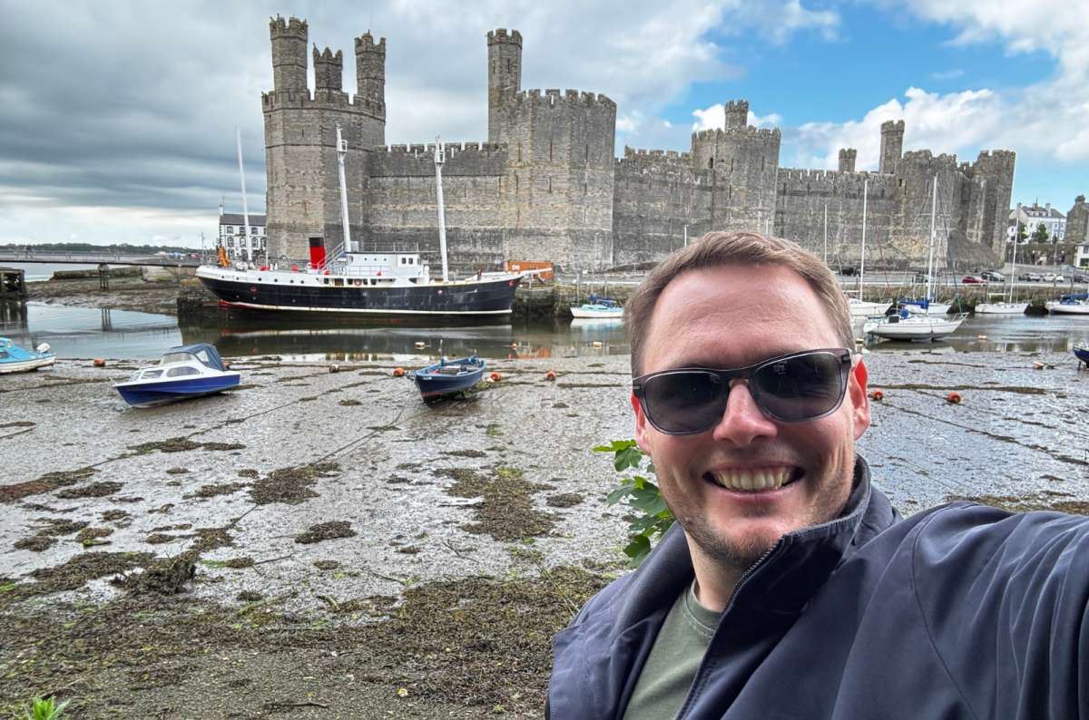 a photo of a tourist taking a selfie in front of Caernarfon Castle, Wales, photo by Next Level of Travel