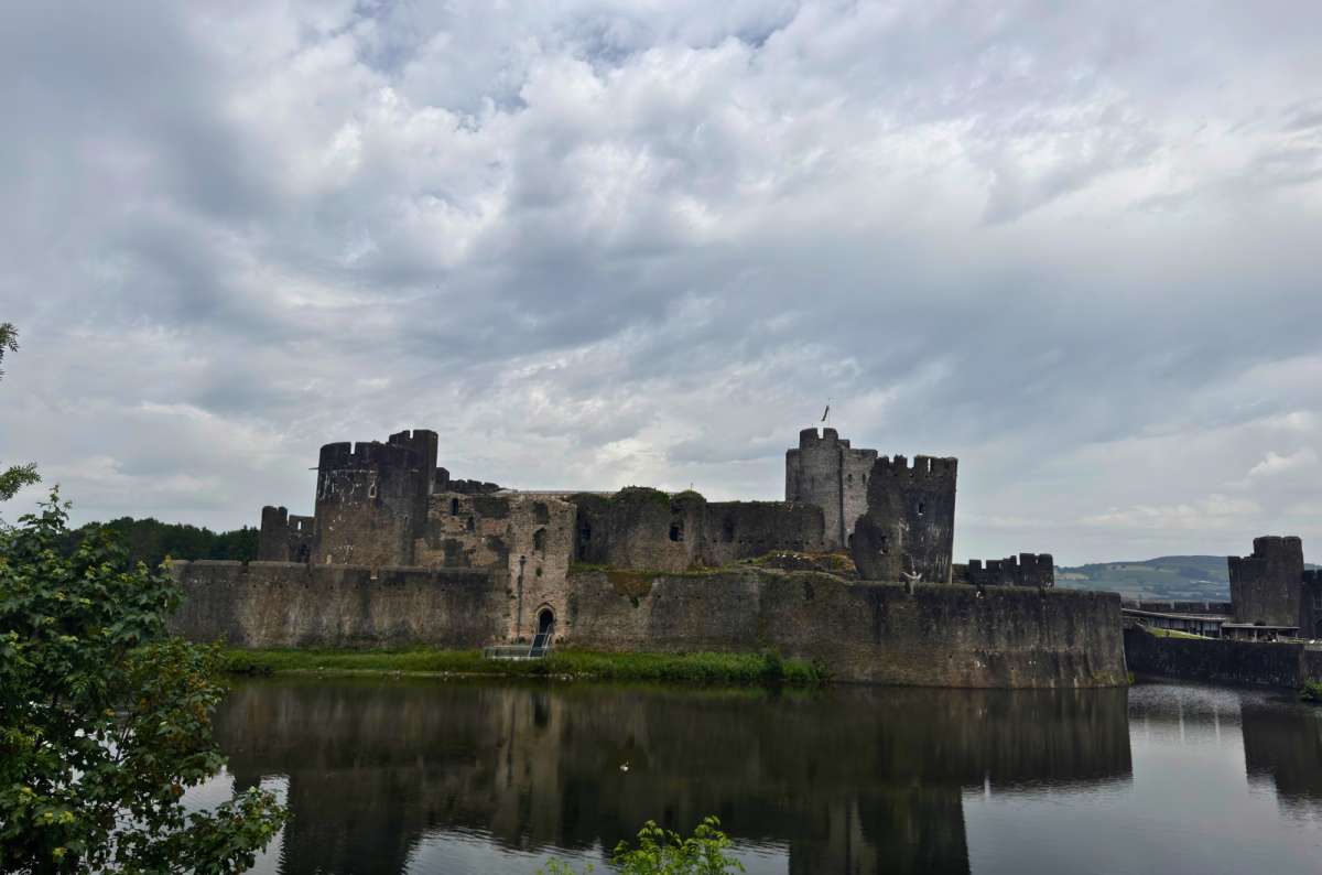 a photo of Caerphilly Castle reflected in its moat under a cloudy sky, Caerphilly, Wales, photo by Next Level of Travel