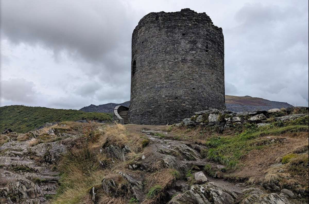 a photo of the round stone keep of Dolbadarn Castle with slate quarries behind, Llanberis, Wales