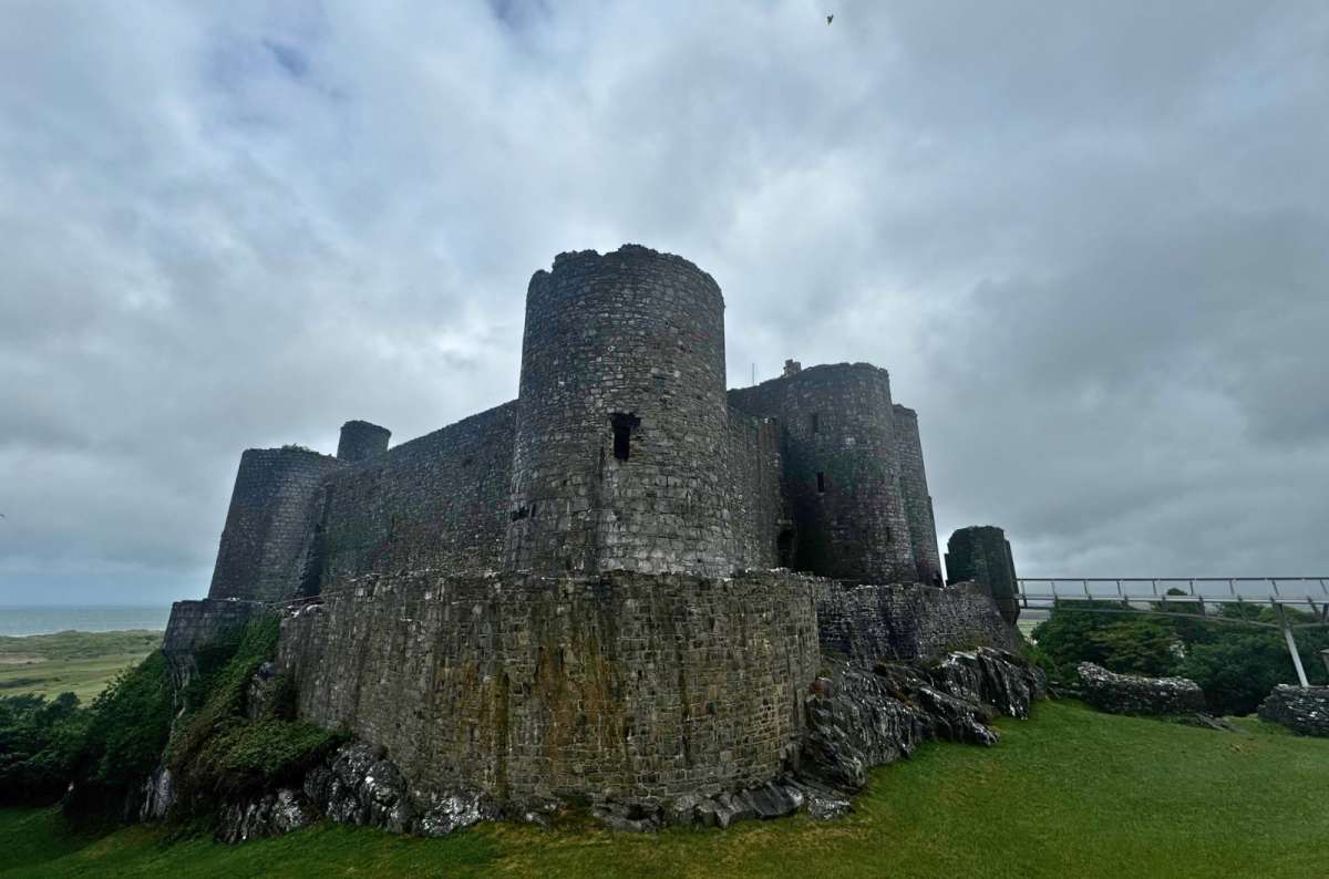 a photo of the round towers of Harlech Castle on a rocky outcrop under a cloudy sky, Harlech, Wales, photo by Next Level of Travel