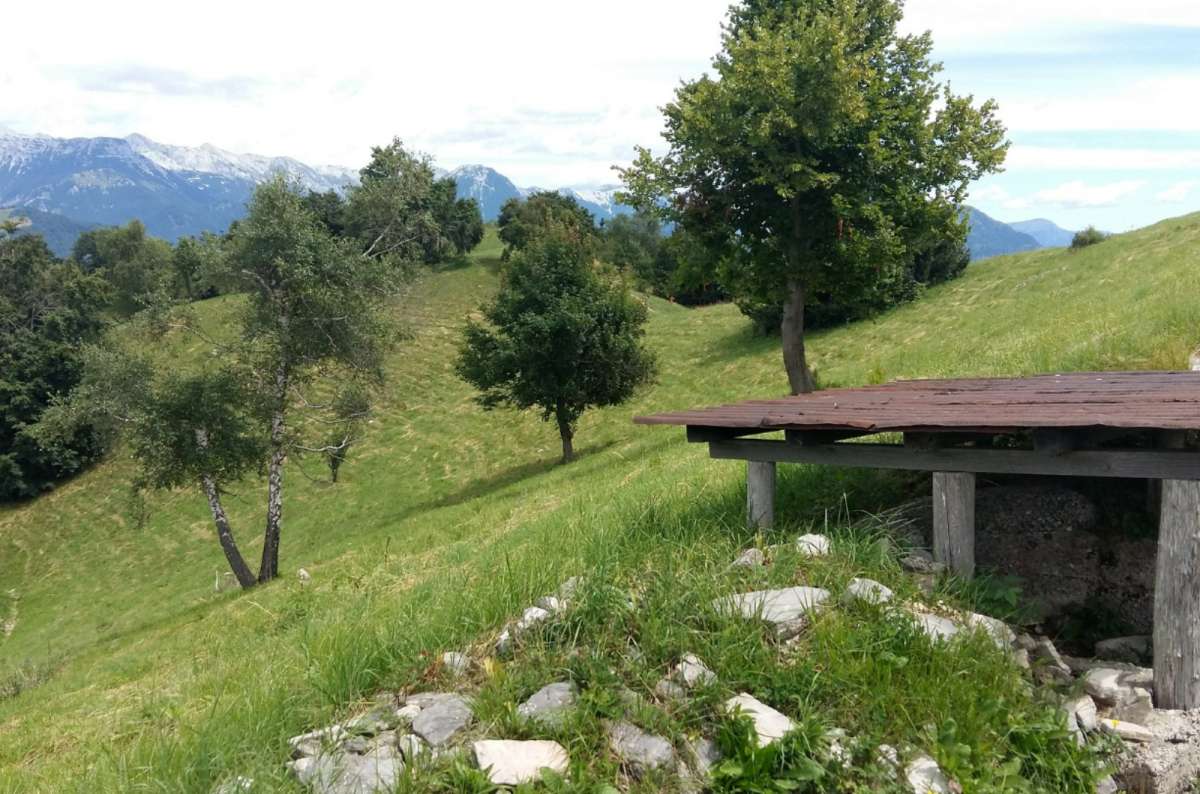 a photo of a roofed WWI trench position on a grassy ridge with snowy peaks behind, Kolovrat Outdoor Museum, Slovenia