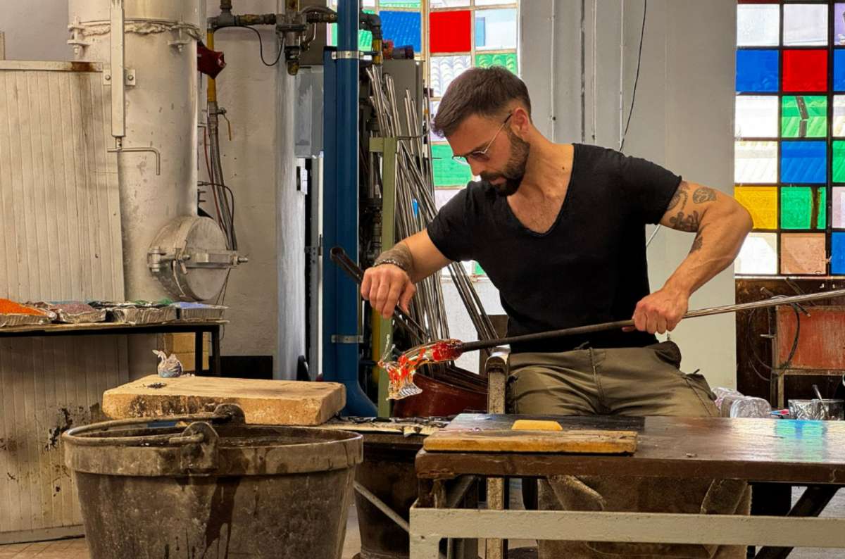 a photo of a glassmaker shaping a red glass figure in a Murano glass factory, Murano, Venice, Italy