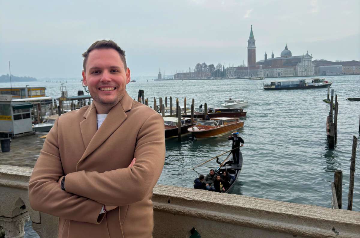 a photo of a tourist on the San Marco waterfront with gondolas, water taxis and San Giorgio Maggiore in the background, Venice, Italy, photo by Next Level of Travel