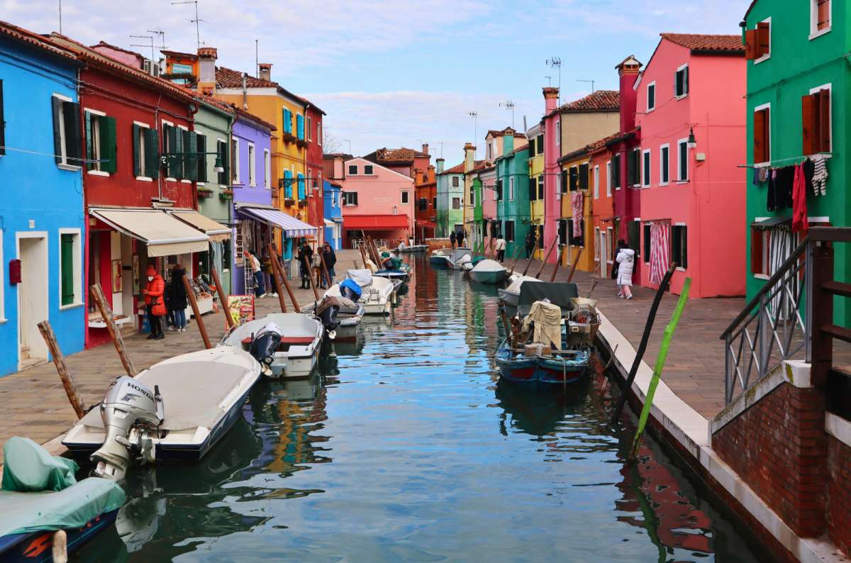 a photo of brightly colored houses and moored boats along a canal on Burano Island