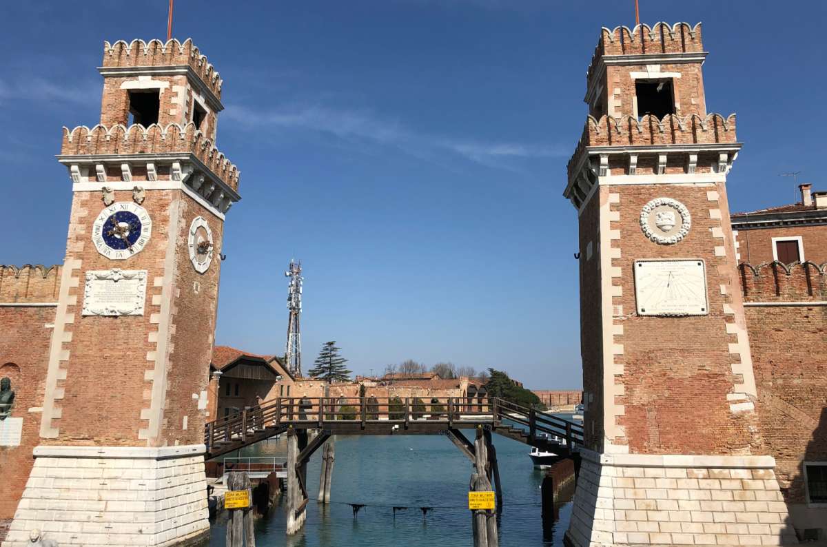 a photo of the two brick towers guarding the water entrance to the Venetian Arsenal with a wooden footbridge between them, Castello, Venice, Italy, photo by Next Level of Travel