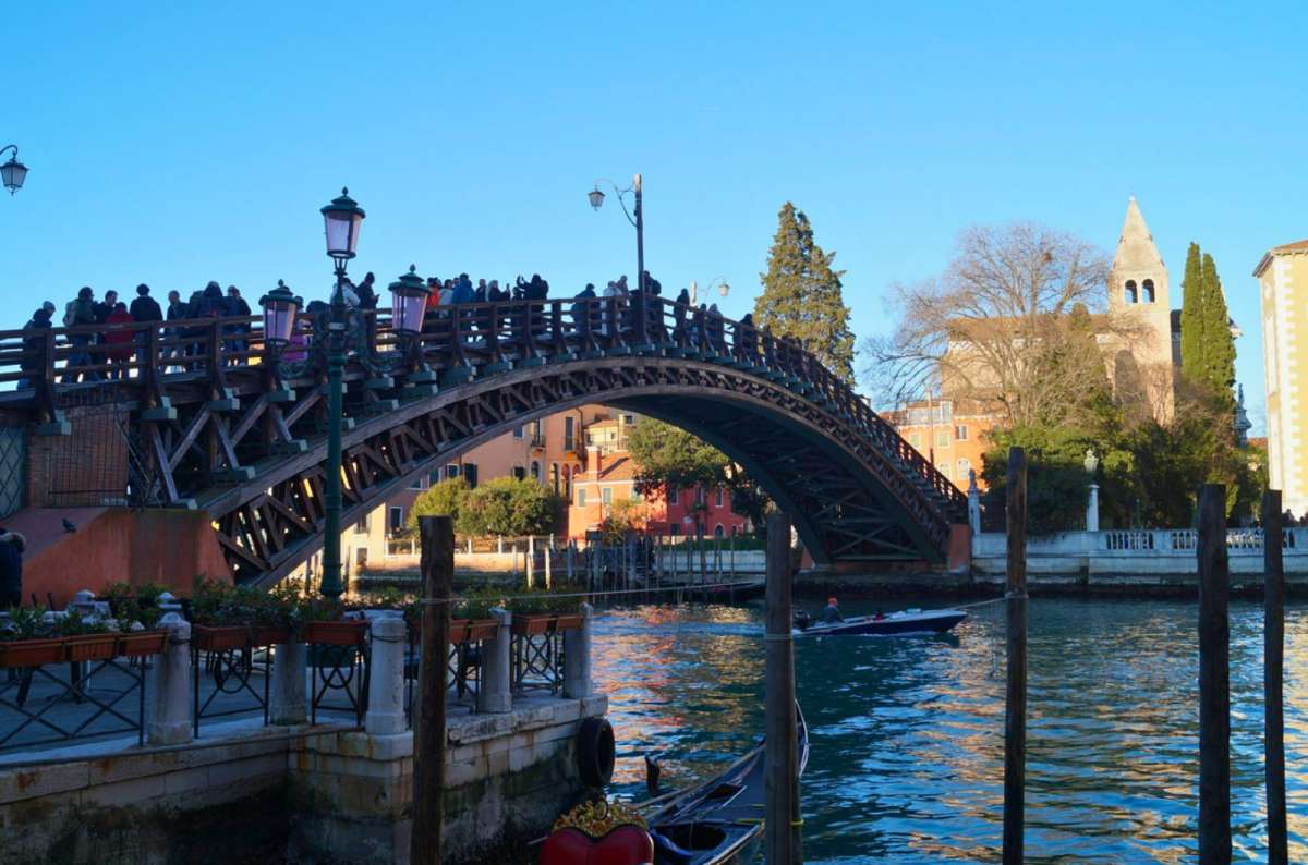 a photo of the wooden Ponte dell’Accademia over the Grand Canal with a gondola in the foreground, Venice, Italy, photo by Next Level of Travel