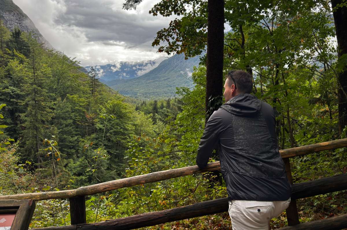 a photo of a tourist leaning on a wooden railing above a forested valley on the Savica trail, Slovenia, photo by Next Level of Travel