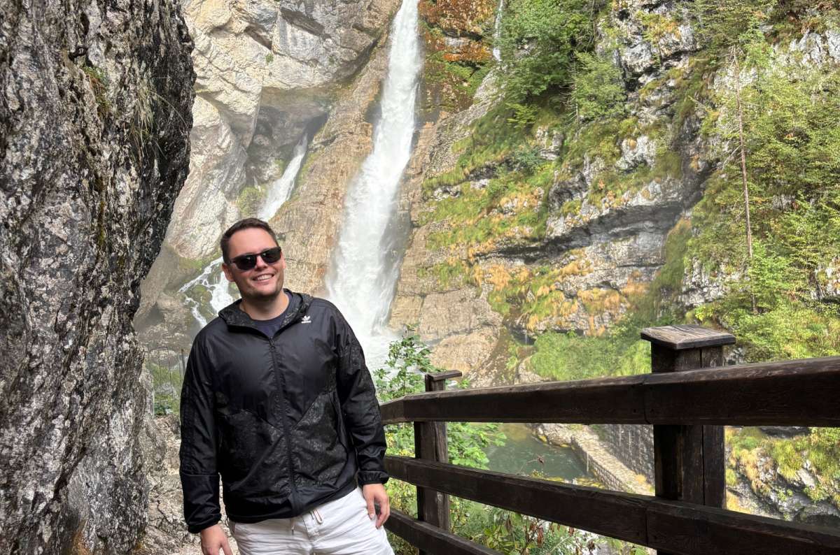 a photo of a tourist standing on the railed stone path in front of Savica Waterfall, Slovenia, photo by Next Level of Travel