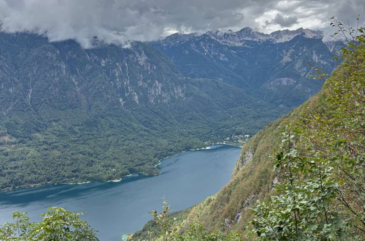 a photo of Lake Bohinj far below the Vogar viewpoint with clouds over the Julian Alps, Slovenia, photo by Next Level of Travel