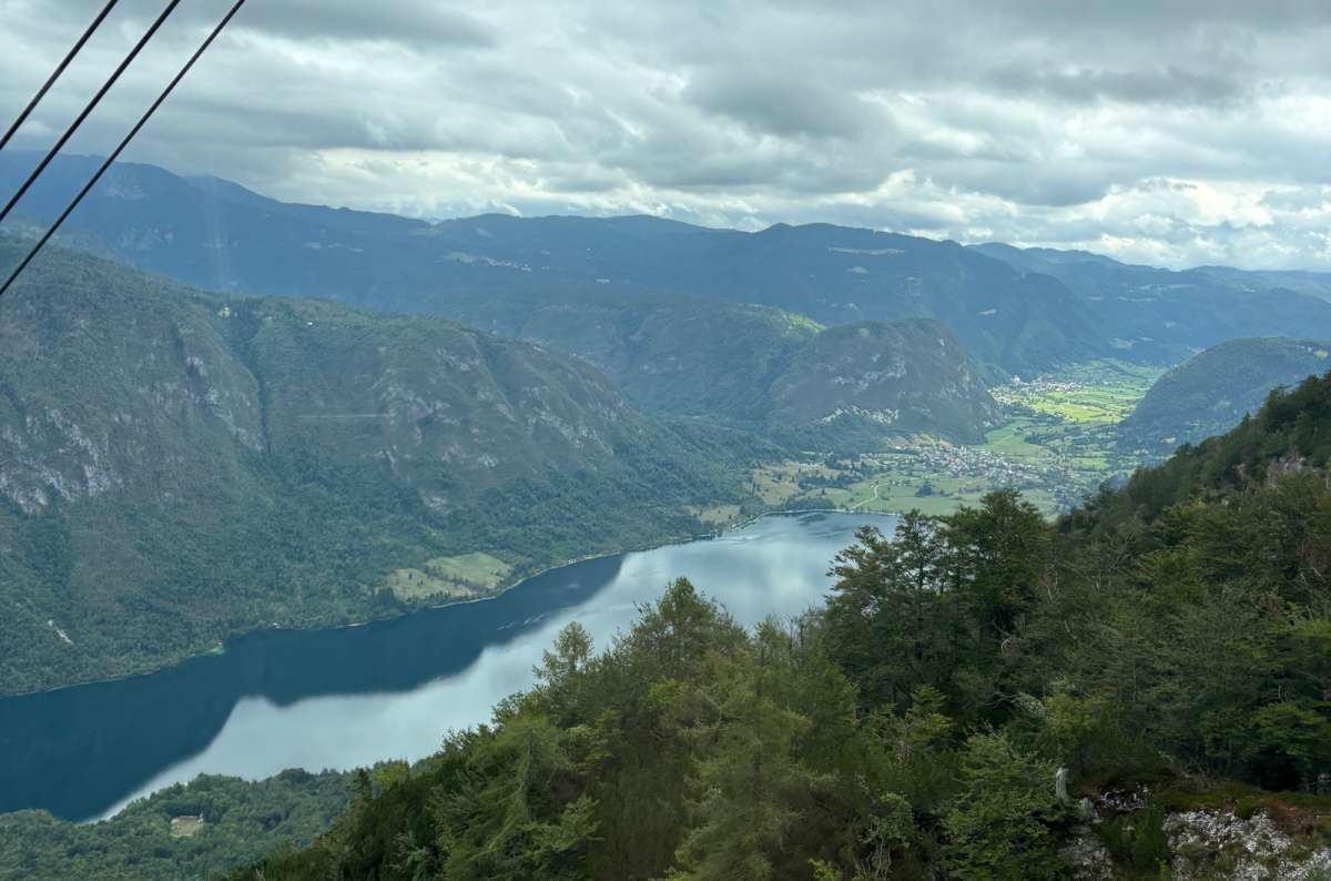 photo of Lake Bohinj and the valley beyond it seen from the Vogel cable car with the cables crossing the sky, Slovenia, photo by Next Level of Travel