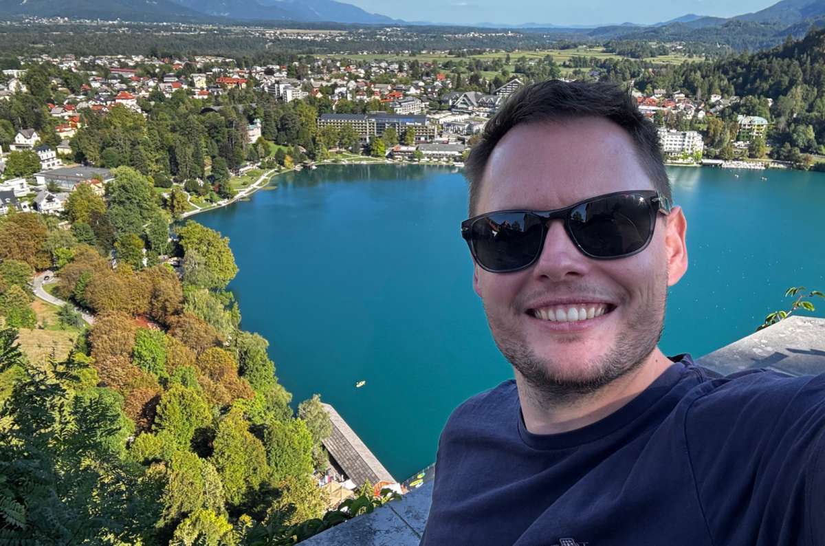 a photo of a tourist taking a selfie with Lake Bled and Bled town below Bled Castle, Slovenia, photo by Next Level of Travel