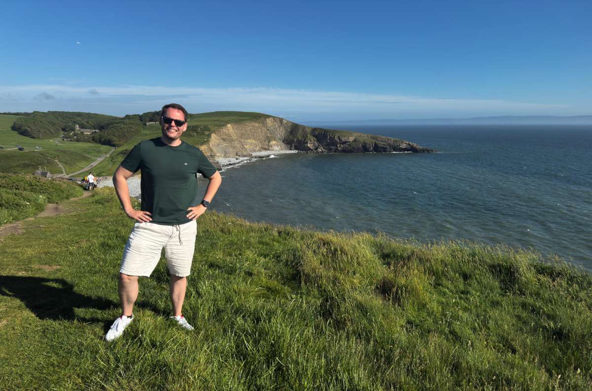a photo of a tourist on the grassy clifftop above Dunraven Bay on a sunny day, Wales, photo by Next Level of Travel
