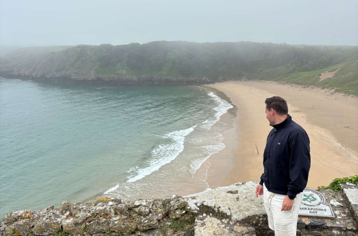 a photo of a tourist on the stone wall above Barafundle Bay on a misty day,Wales, photo by Next Level of Travel
