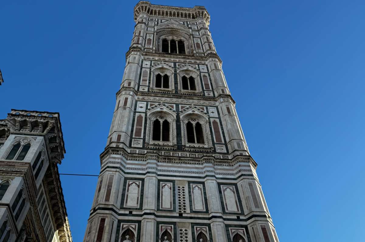 a photo looking up at the marble-clad Giotto's Bell Tower against a blue sky, Florence, Italy, photo by Next Level of Travel