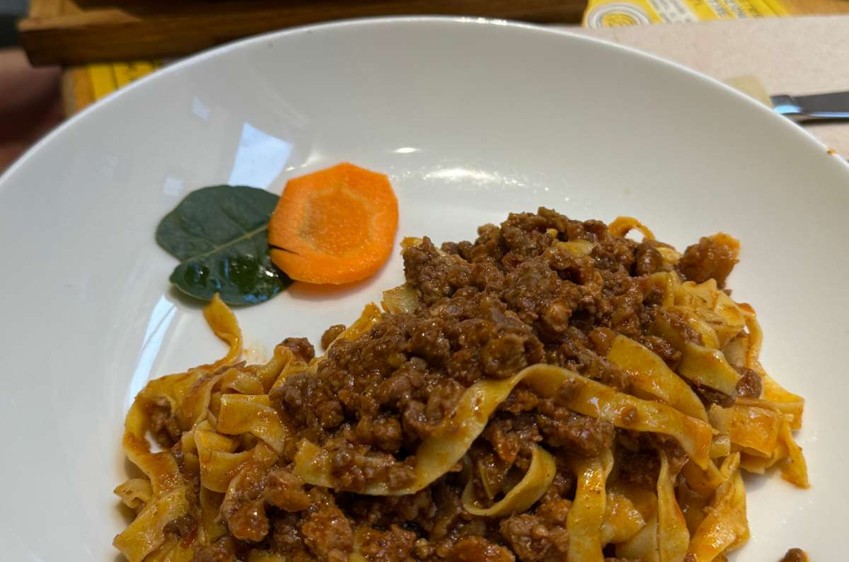 a photo of a plate of tagliatelle al ragù on a restaurant table, Bologna, Italy, photo by Next Level of Travel