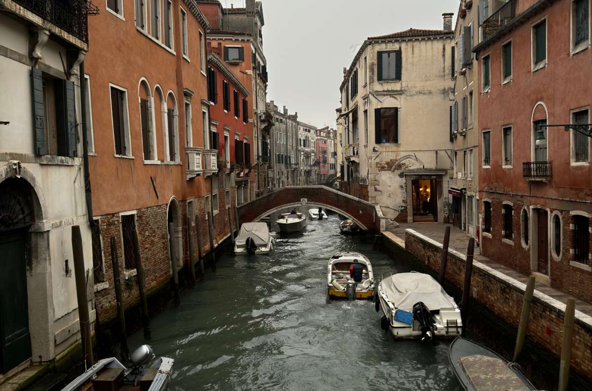 a photo of a quiet canal lined with boats and old houses leading to a small bridge, Venice, Italy, photo by Next Level of Travel