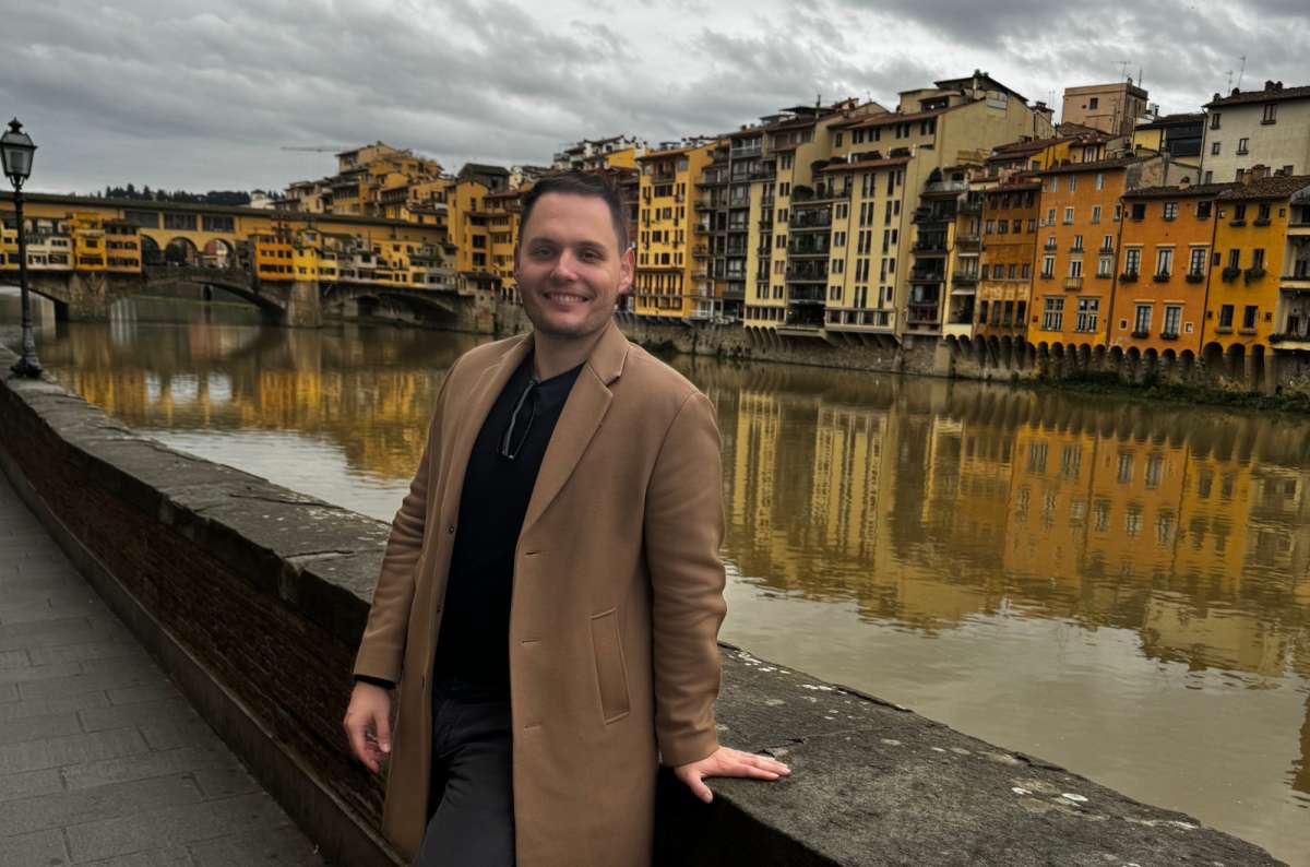 a photo of a tourist leaning on the riverside wall of the Arno with Ponte Vecchio in the background, Florence, Italy, photo by Next Level of Travel