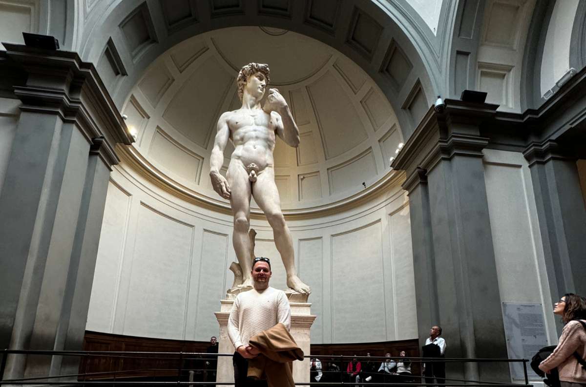 a photo of a tourist standing in front of Michelangelo's David in the domed tribune of the Accademia Gallery, Florence, Italy, photo by Next Level of Travel