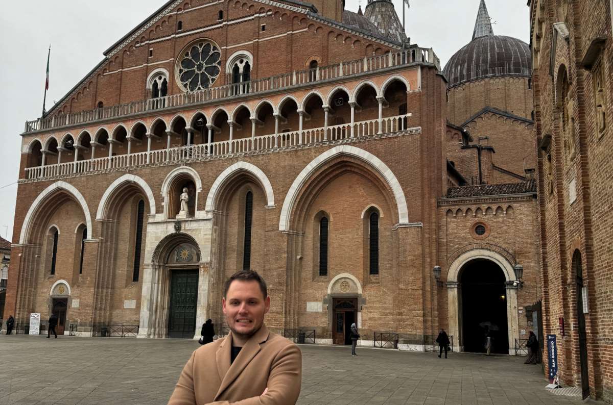 a photo of a tourist standing in front of the brick Basilica of Saint Anthony with its domes, Padua, Italy, photo by Next Level of Travel