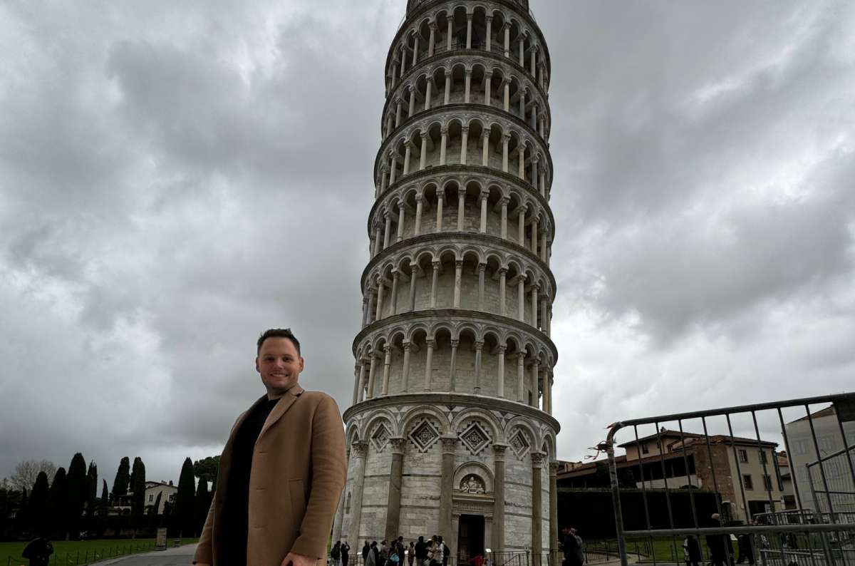 a photo of a tourist standing in front of the Leaning Tower of Pisa under a stormy sky, Pisa, Italy, photo by Next Level of Travel