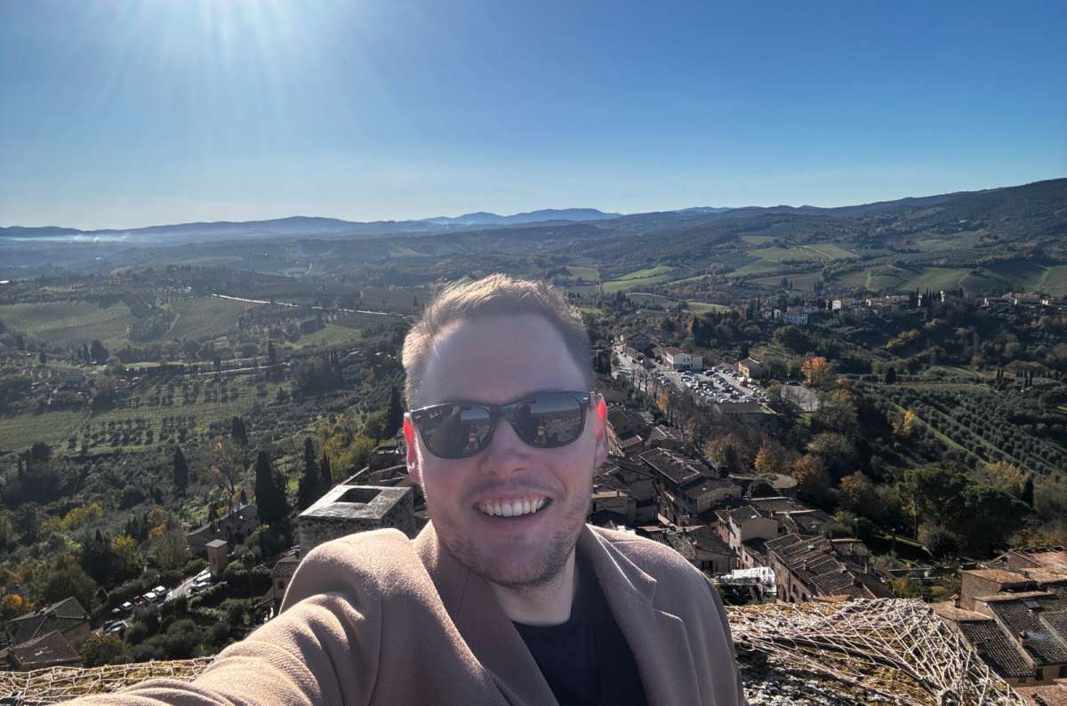 a photo of a tourist taking a selfie at the top of Torre Grossa with the rolling Tuscan hills behind, San Gimignano, Italy, photo by Next Level of Travel