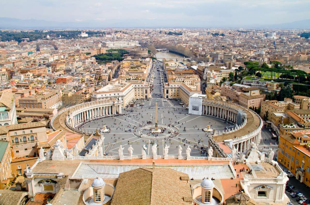 a photo of St. Peter's Square and its colonnades seen from above with Rome stretching to the horizon, Vatican City
