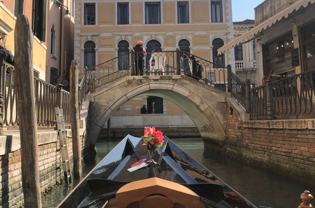 a photo of the bow of a gondola gliding along a narrow canal towards a stone bridge, Venice, Italy, photo by Next Level of Travel