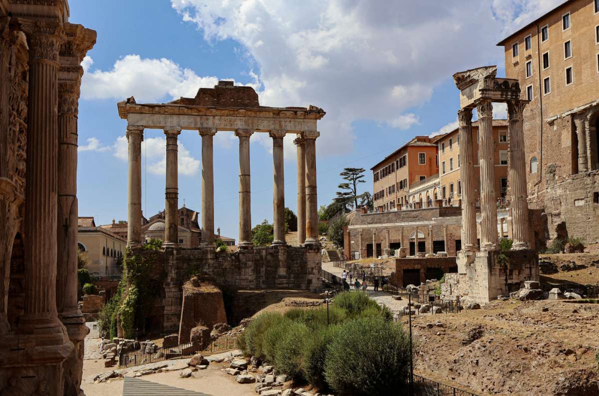 a photo of the columns of the Temple of Saturn among the ruins of the Roman Forum under a blue sky, Rome, Italy