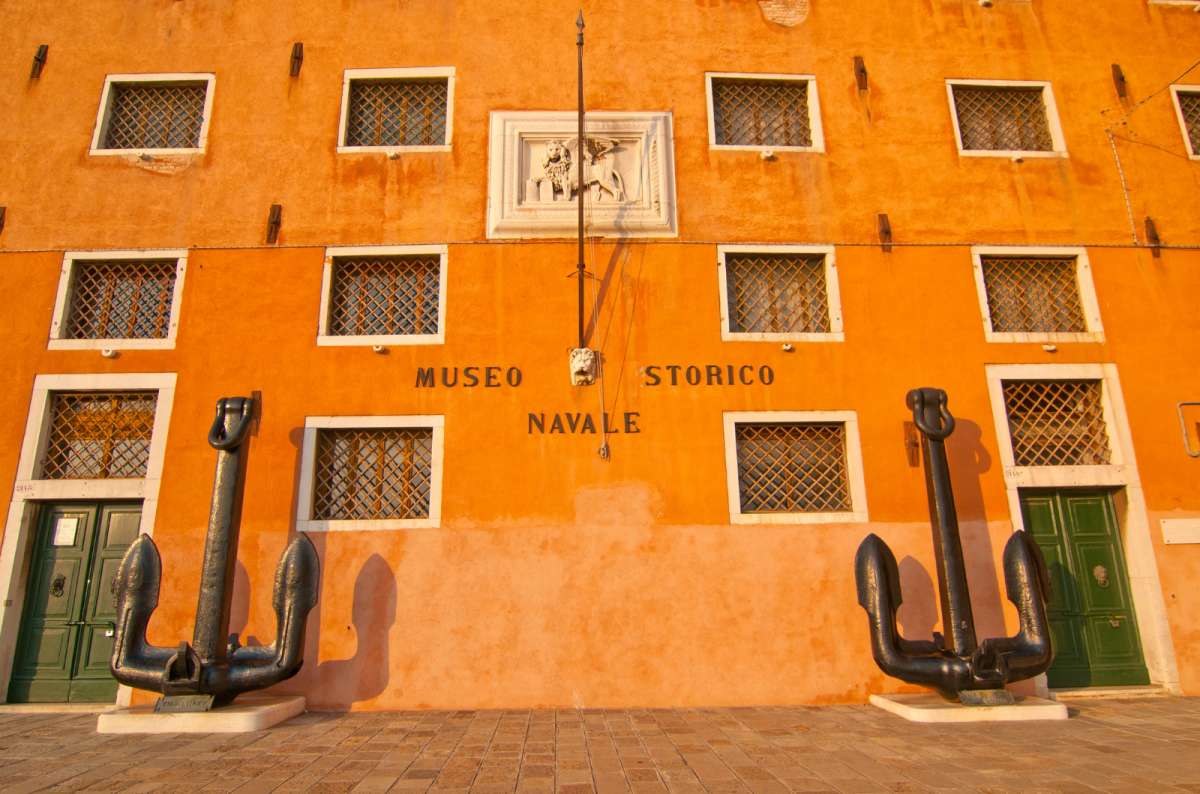 a photo of the orange facade of the Museo Storico Navale with two large anchors at the entrance, Castello, Venice, Italy