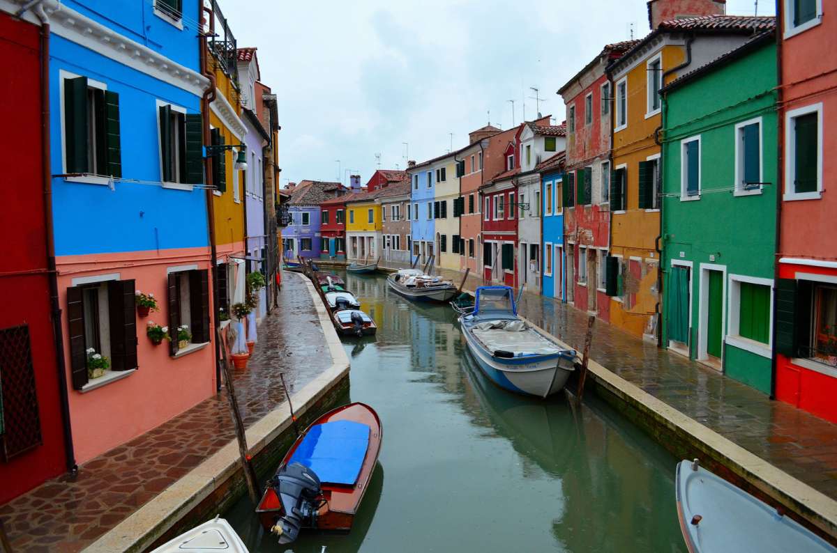 a photo of colorful houses along a canal with moored boats on a rainy day on Burano, Venice, Italy