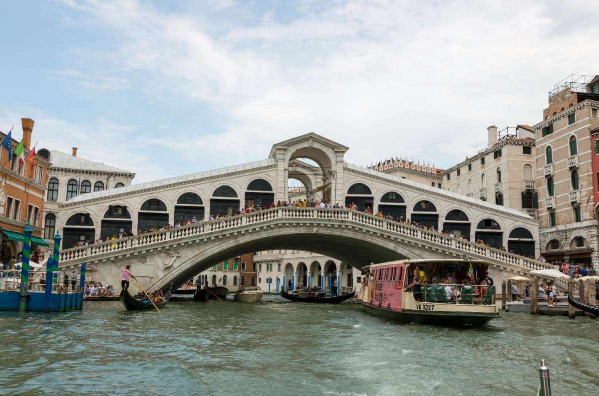 a photo of the Rialto Bridge over the Grand Canal with a vaporetto and gondolas passing beneath it, Venice, Italy
