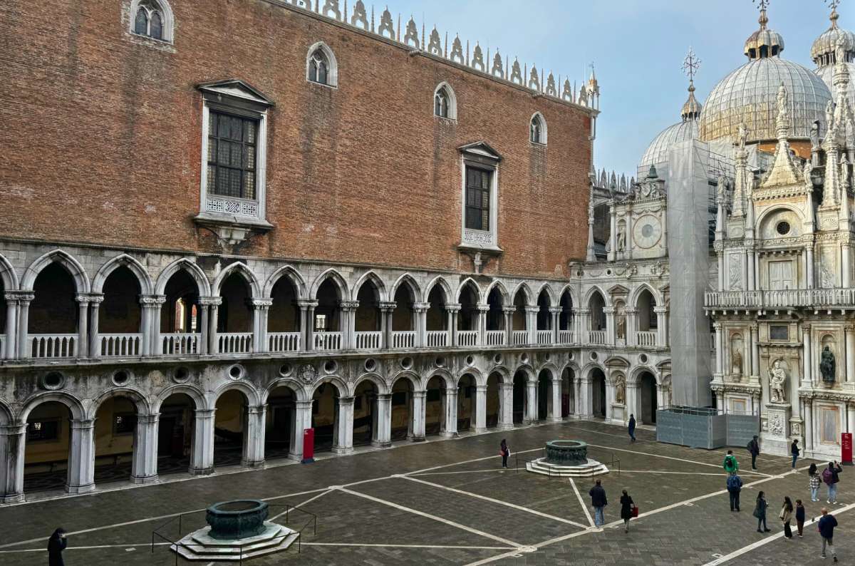 photo of the courtyard of Doge’s Palace with its Gothic arcades, two bronze wellheads and the domes of St. Mark’s Basilica behind, Venice, Italy, photo by Next Level of Travel