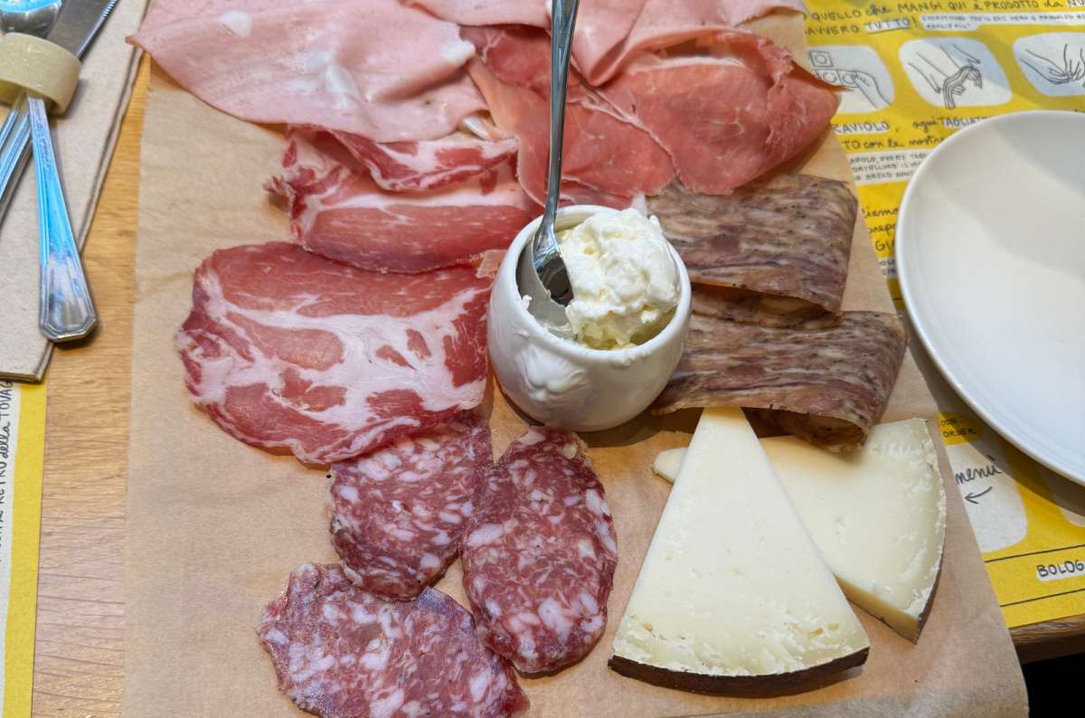 a photo of a board of mortadella, salami, coppa and cheese on a restaurant table, Bologna, Italy, photo by Next Level of Travel