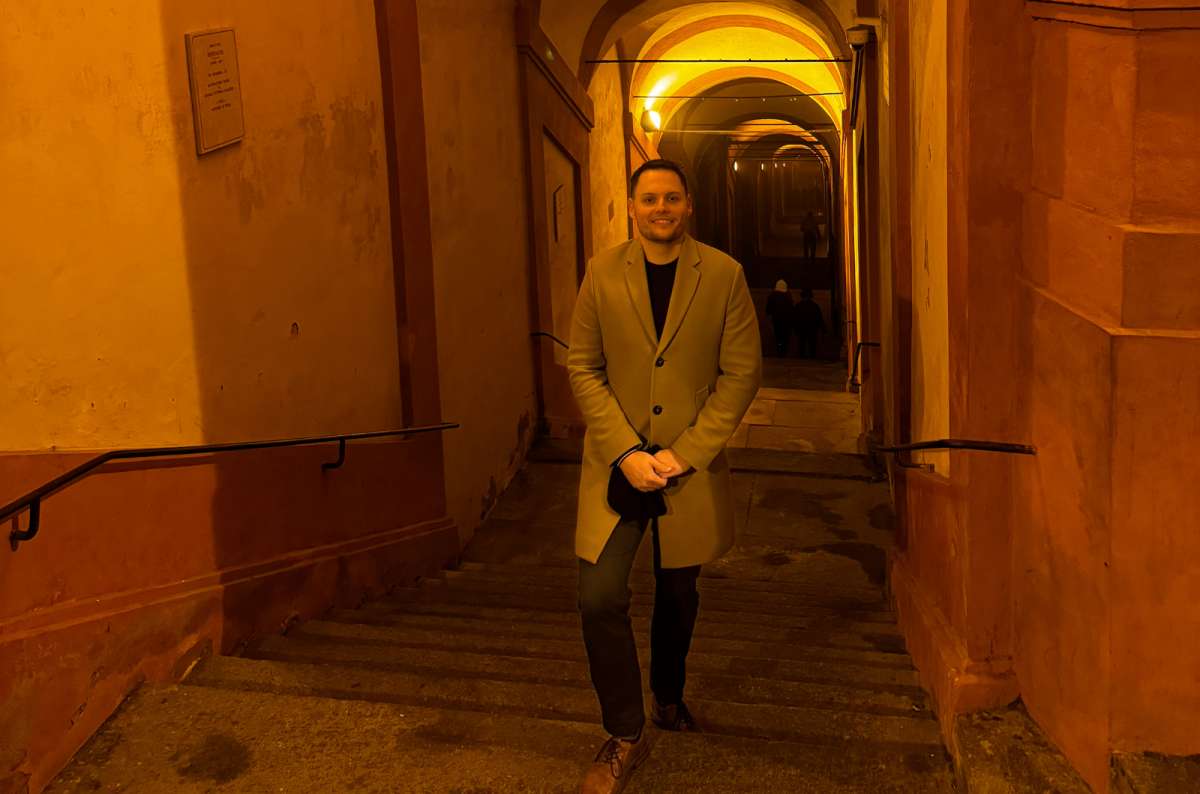 a photo of a tourist climbing the stairs under the lit arches of the San Luca portico at night, Bologna, Italy, photo by Next Level of Travel