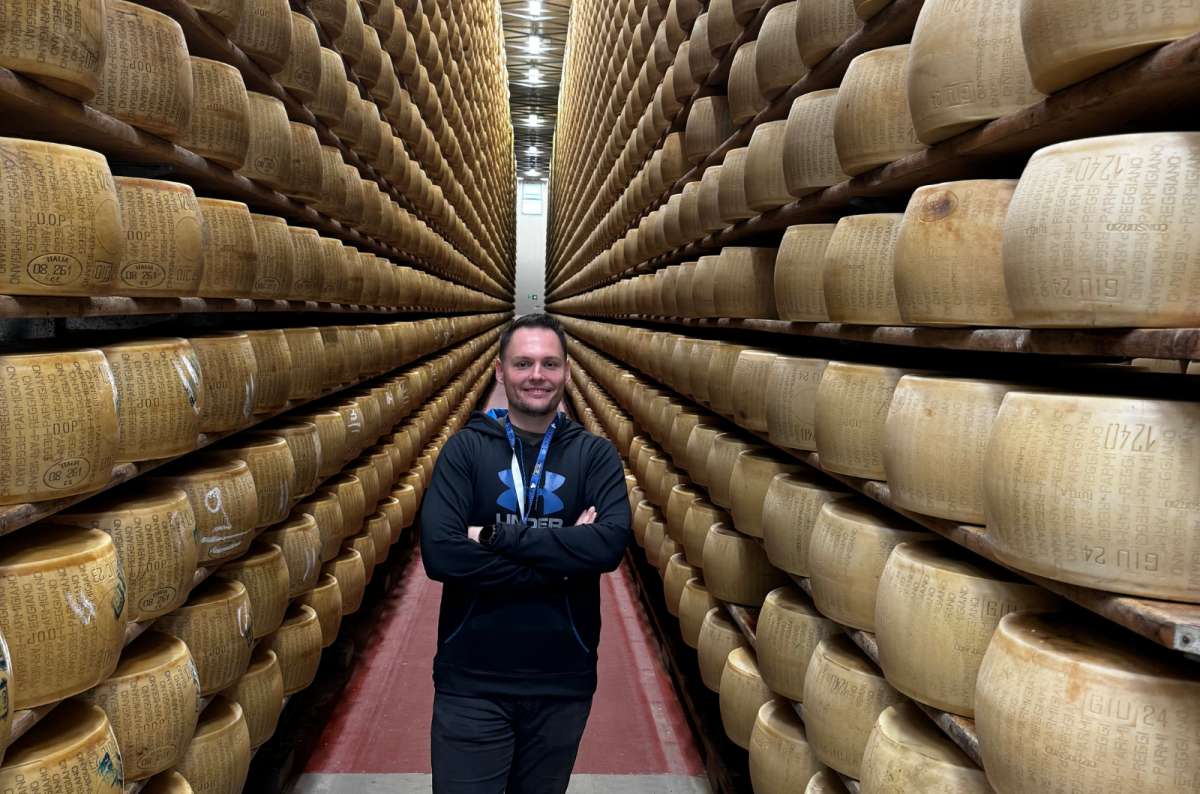 a photo of a tourist standing in a long aisle between towering shelves of Parmigiano Reggiano wheels at the 4 Madonne dairy, Modena, Italy, photo by Next Level of Travel