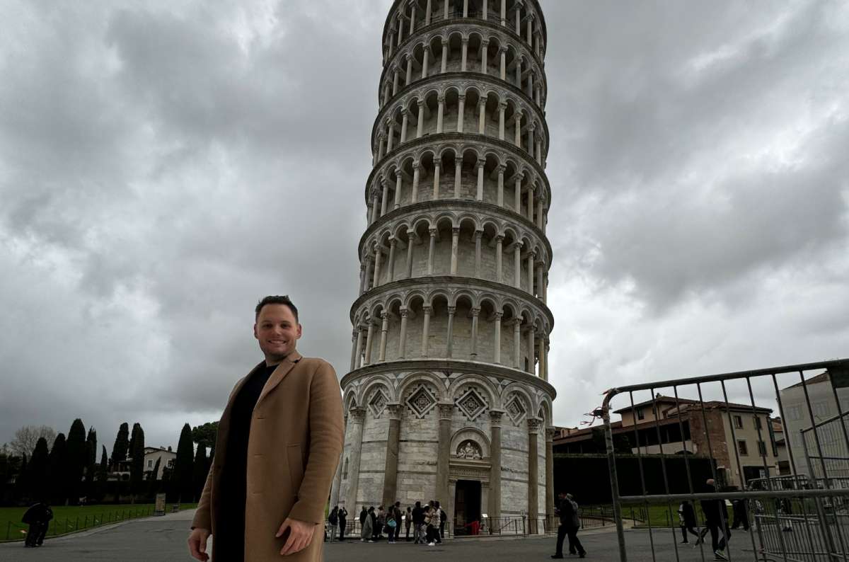 a photo of a tourist standing in front of the Leaning Tower of Pisa under a cloudy sky, Pisa, Italy, photo by Next Level of Travel