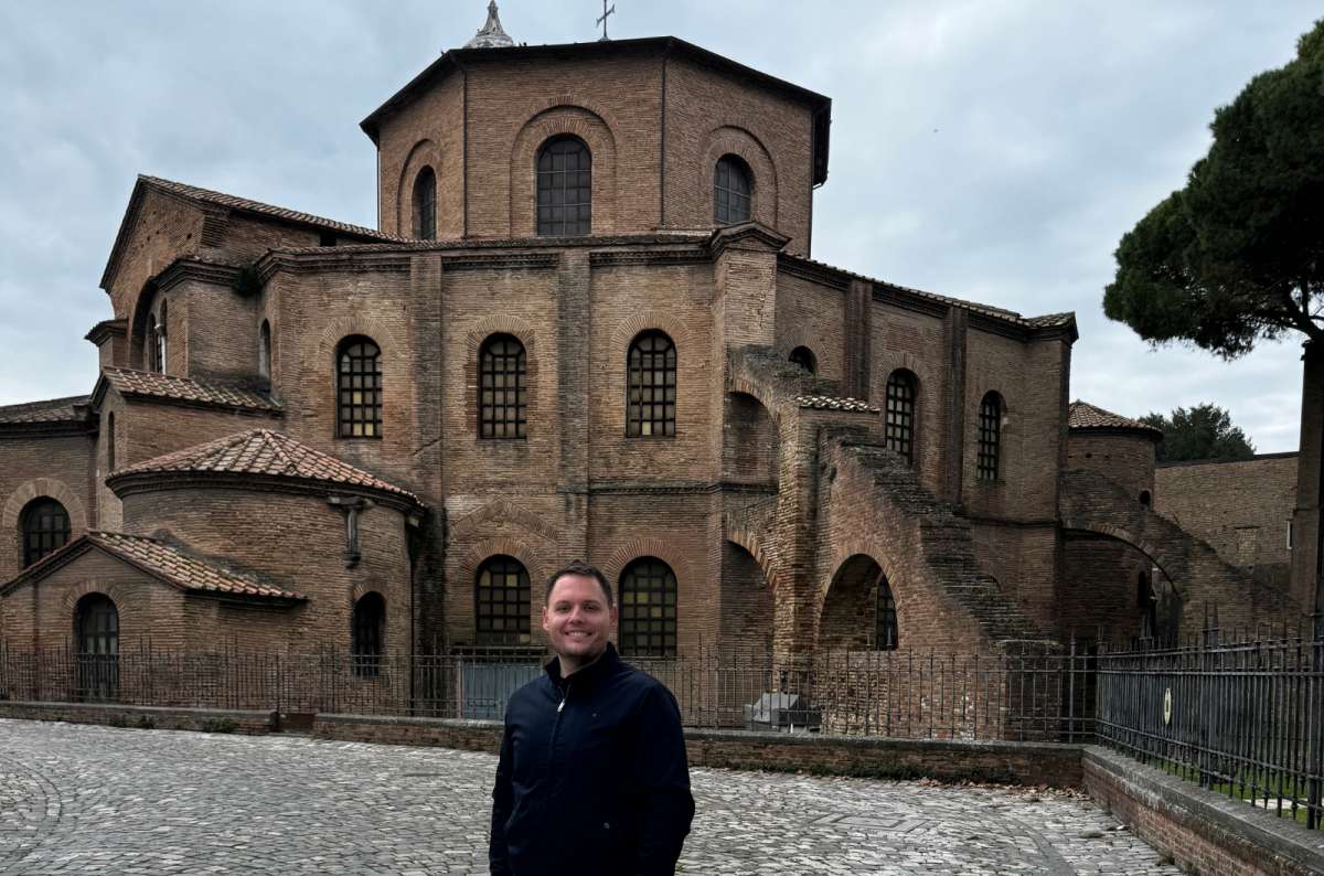 a photo of a tourist standing on the cobbled courtyard in front of the brick Basilica of San Vitale, Ravenna, Italy, photo by Next Level of Travel